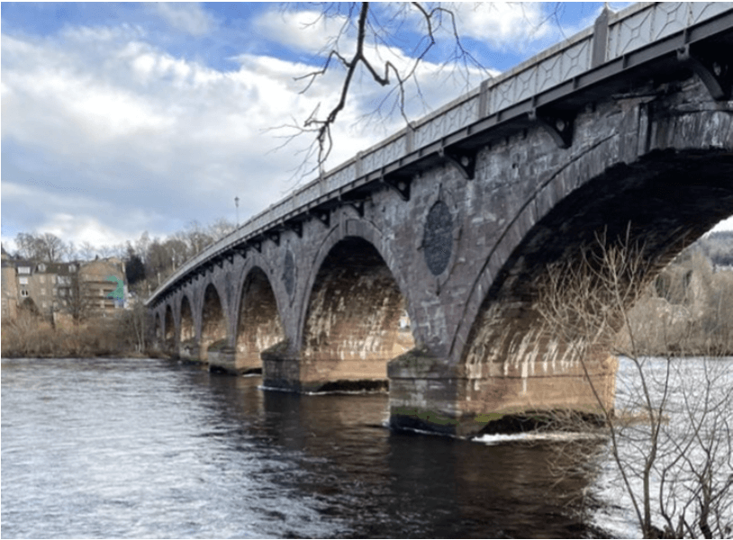 A bridge over the River Tay with trees and buildings in the background