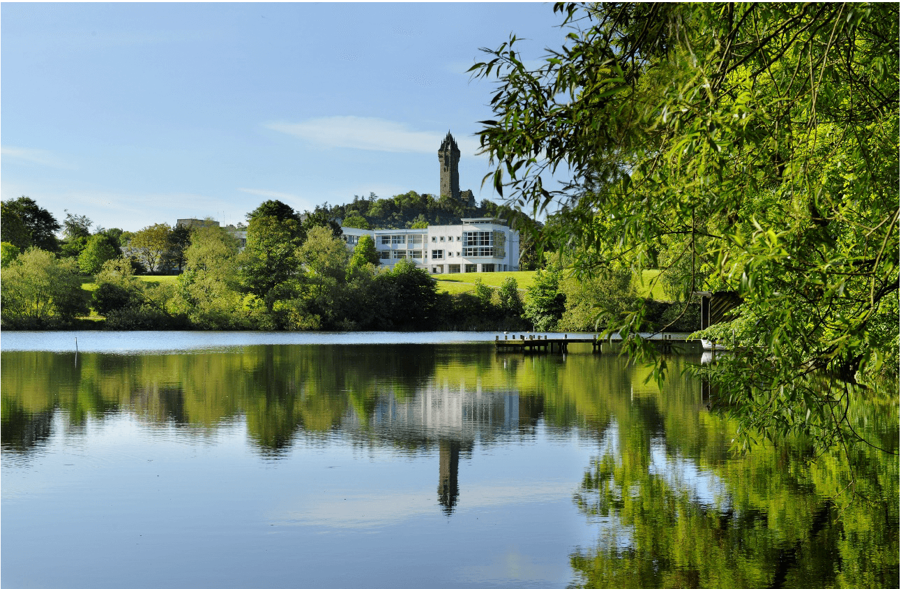 A body of water with trees and a University of Stirling building in the background.