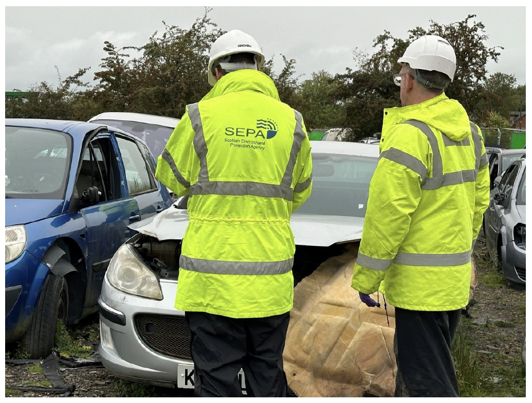 Two workers from SEPA in reflective jackets looking at a car dumped illegally.