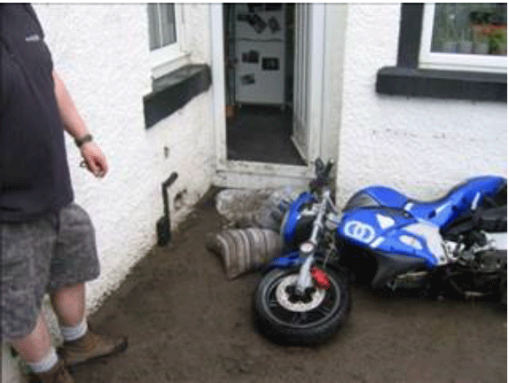 A person standing next to a motorcycle outside a house that has been flooded.