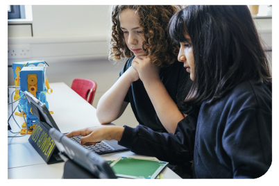 Case study: Two school children using a computer tablet to programme Marty the robot, who is sat on the desk beside them