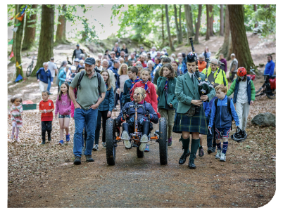 Case study: A large crowd walking through woodland behind a bagpiper as part of the climate festival